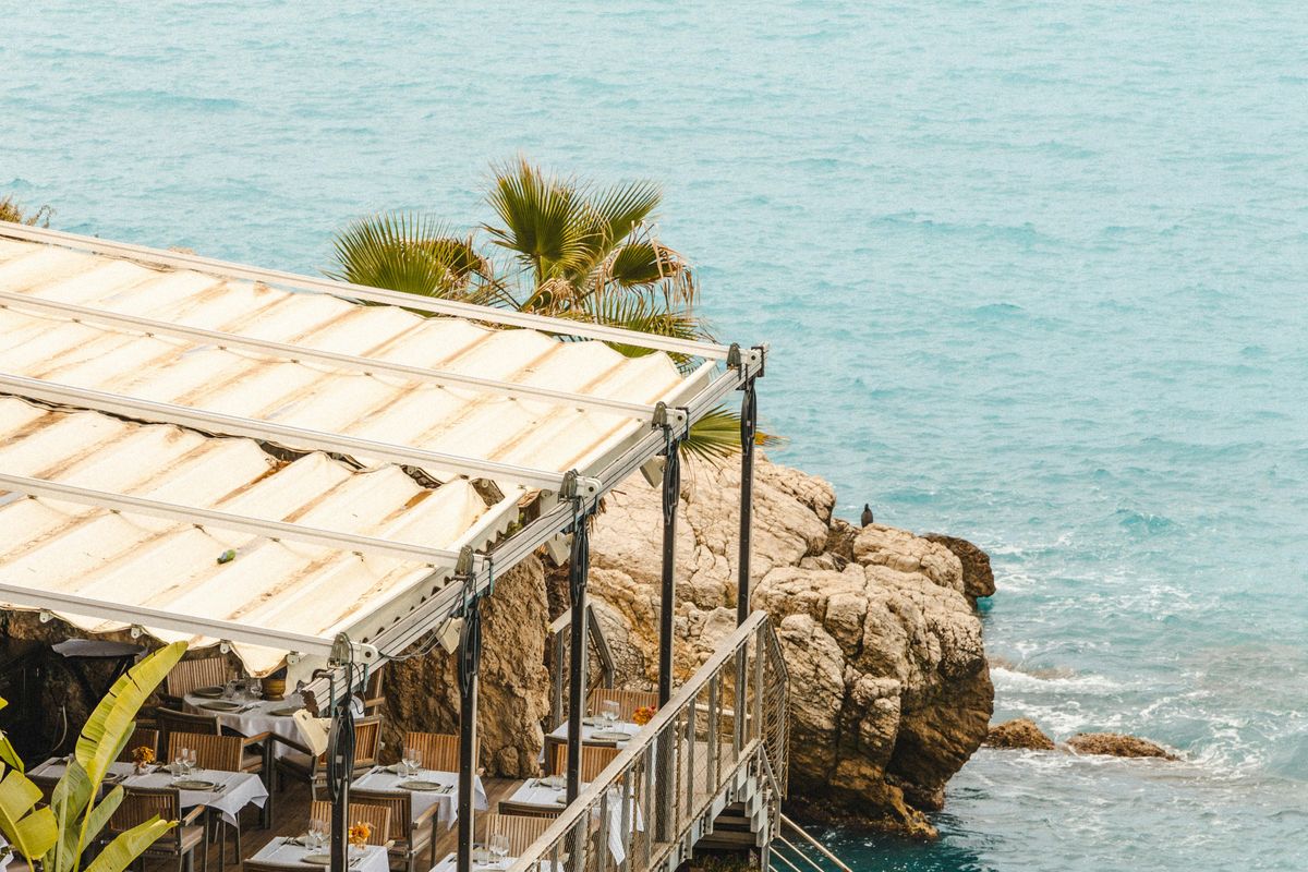 Seafront restaurant terrace on the rocks of the Mediterranean in Nice, turquoise sea in summer