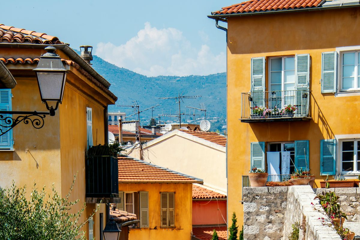 Narrow alleyways with ochre and yellow facades in Old Nice under summer sun, lanterns and colourful shutters